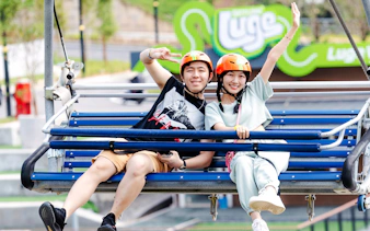 Couple on chairlift at Skyline Luge Kuala Lumpur, wearing helmets and smiling.