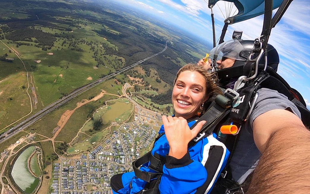Tandem skydive over Sydney with cityscape and greenery below.