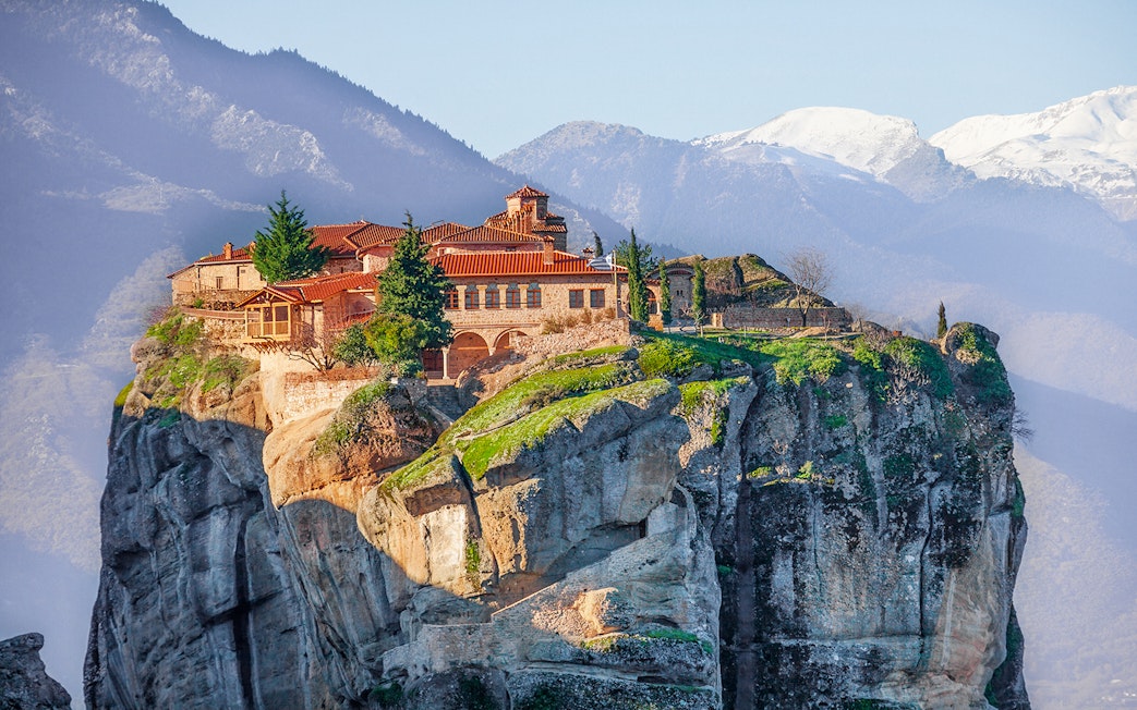 Meteora monastery perched on a cliff with mountains in the background, Greece.