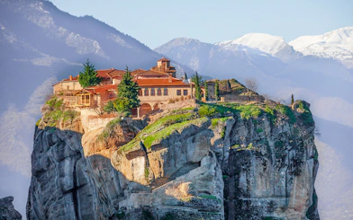 Meteora monastery perched on a cliff with mountains in the background, Greece.