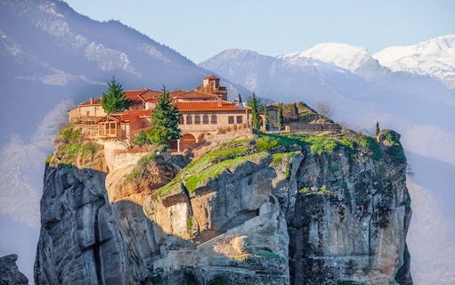 Meteora monastery perched on a cliff with mountains in the background, Greece.