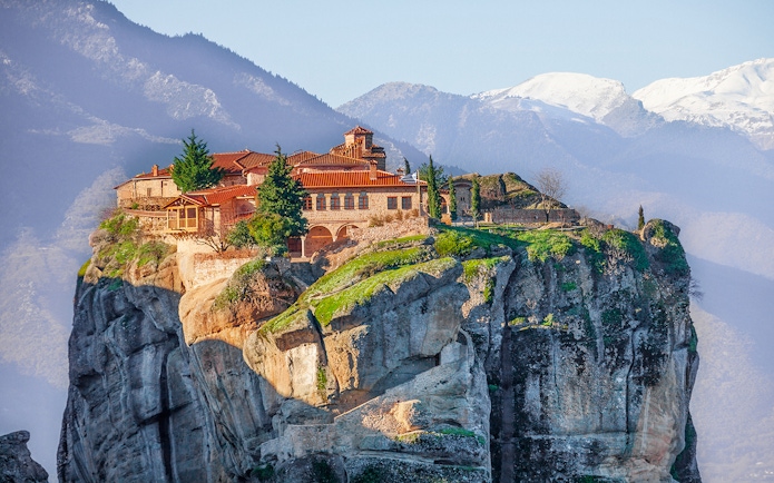 Meteora monastery perched on a cliff with mountains in the background, Greece.