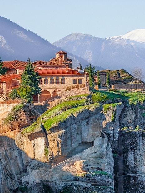 Meteora monastery perched on a cliff with mountains in the background, Greece.
