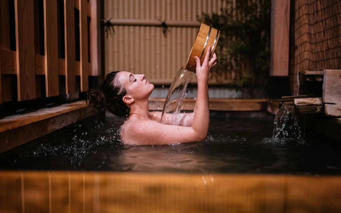 Woman relaxing in a Japanese onsen bath with wooden tub, Japan wellness spa experience.