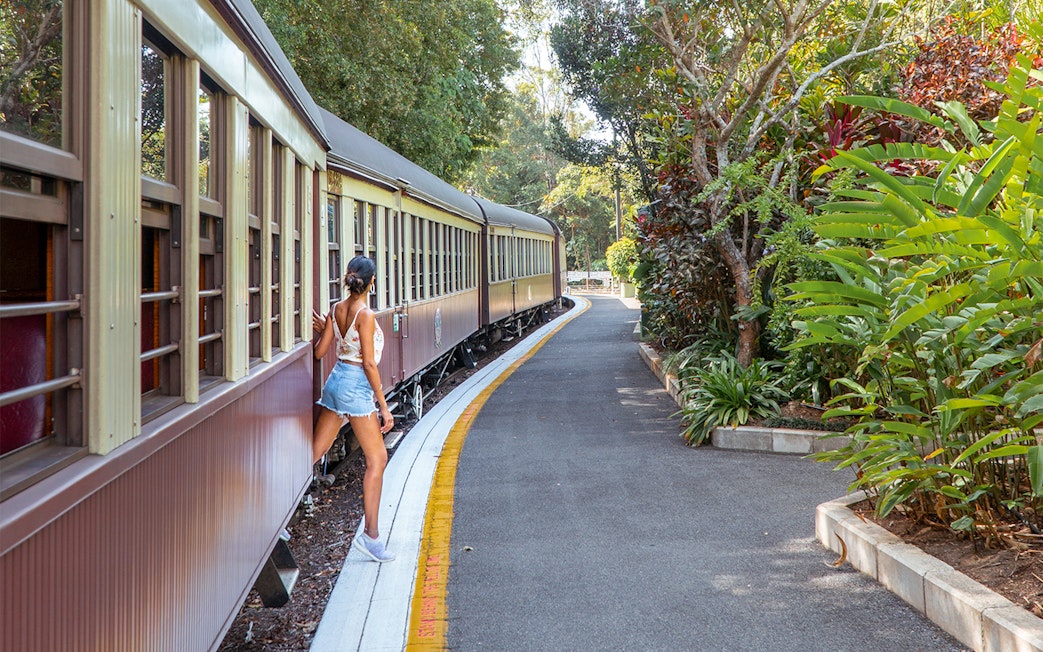 Tourist stepping off Kuranda Scenic Rail surrounded by lush greenery.