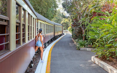 Tourist stepping off Kuranda Scenic Rail surrounded by lush greenery.