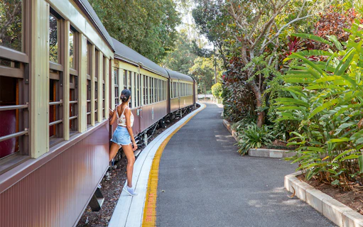 Tourist stepping off Kuranda Scenic Rail surrounded by lush greenery.