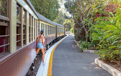 Tourist stepping off Kuranda Scenic Rail surrounded by lush greenery.