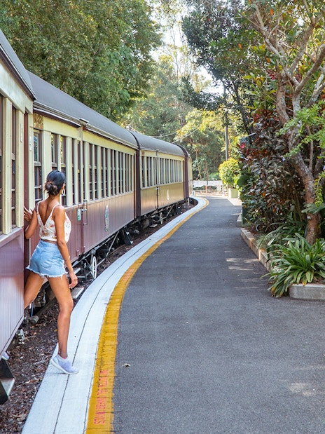 Tourist stepping off Kuranda Scenic Rail surrounded by lush greenery.