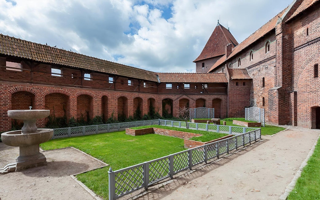 Courtyard of Malbork Castle with brick walls and a stone fountain, seen on a tour from Gdańsk.
