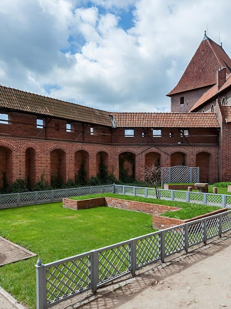 Courtyard of Malbork Castle with brick walls and a stone fountain, seen on a tour from Gdańsk.