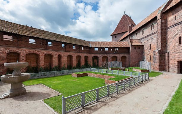 Courtyard of Malbork Castle with brick walls and a stone fountain, seen on a tour from Gdańsk.