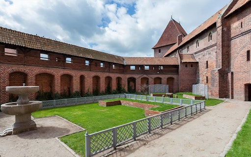 Malbork Castle courtyard with brick walls and a stone fountain, part of the audio guide tour from Gdańsk.