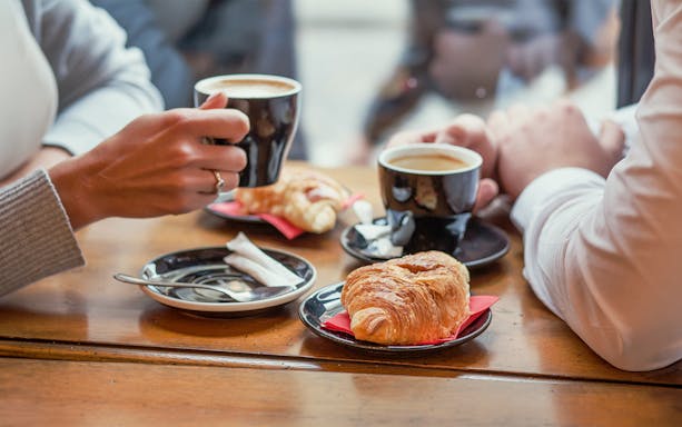 Two people enjoying coffee and croissants on a Seine River cruise in Paris.