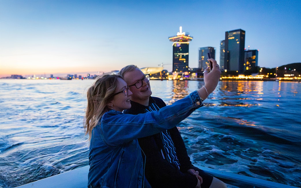 Couple taking a selfie on the Happy Valentine Evening Cruise with city skyline in the background.