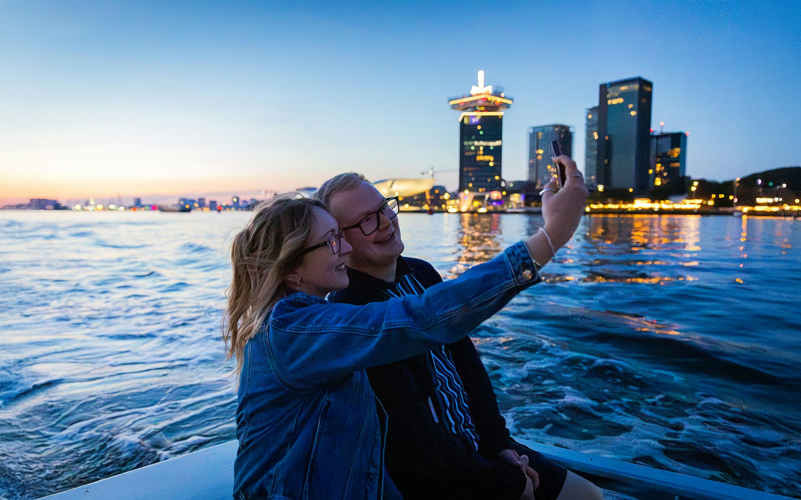Couple taking a selfie on the Happy Valentine Evening Cruise with city skyline in the background.