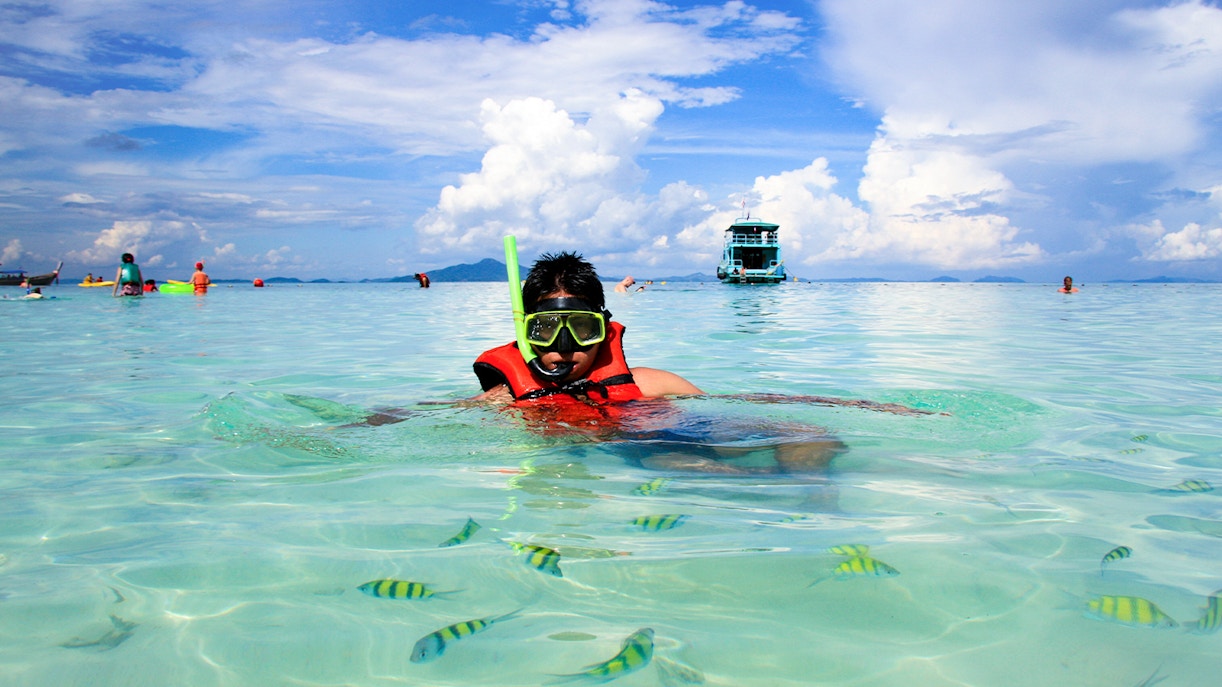 Young man snorkeling in clear waters at Phi Phi Island, Thailand, surrounded by vibrant marine life.