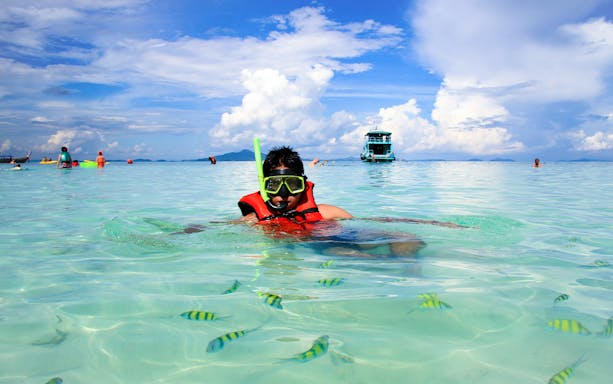 Young man snorkeling in clear waters at Phi Phi Island, Thailand with tropical fish.