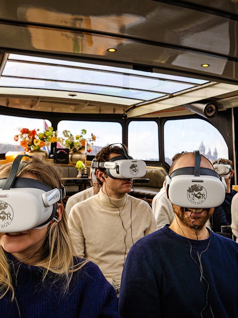 Tourists wearing VR headsets on a luxury boat in Amsterdam canal.