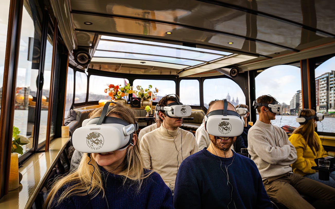 Tourists wearing VR headsets on a luxury boat in Amsterdam canal.