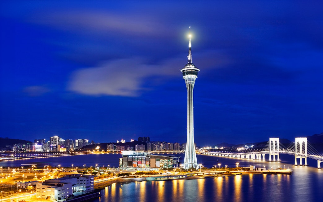 Macau Tower illuminated at night with city skyline and bridge in the background.