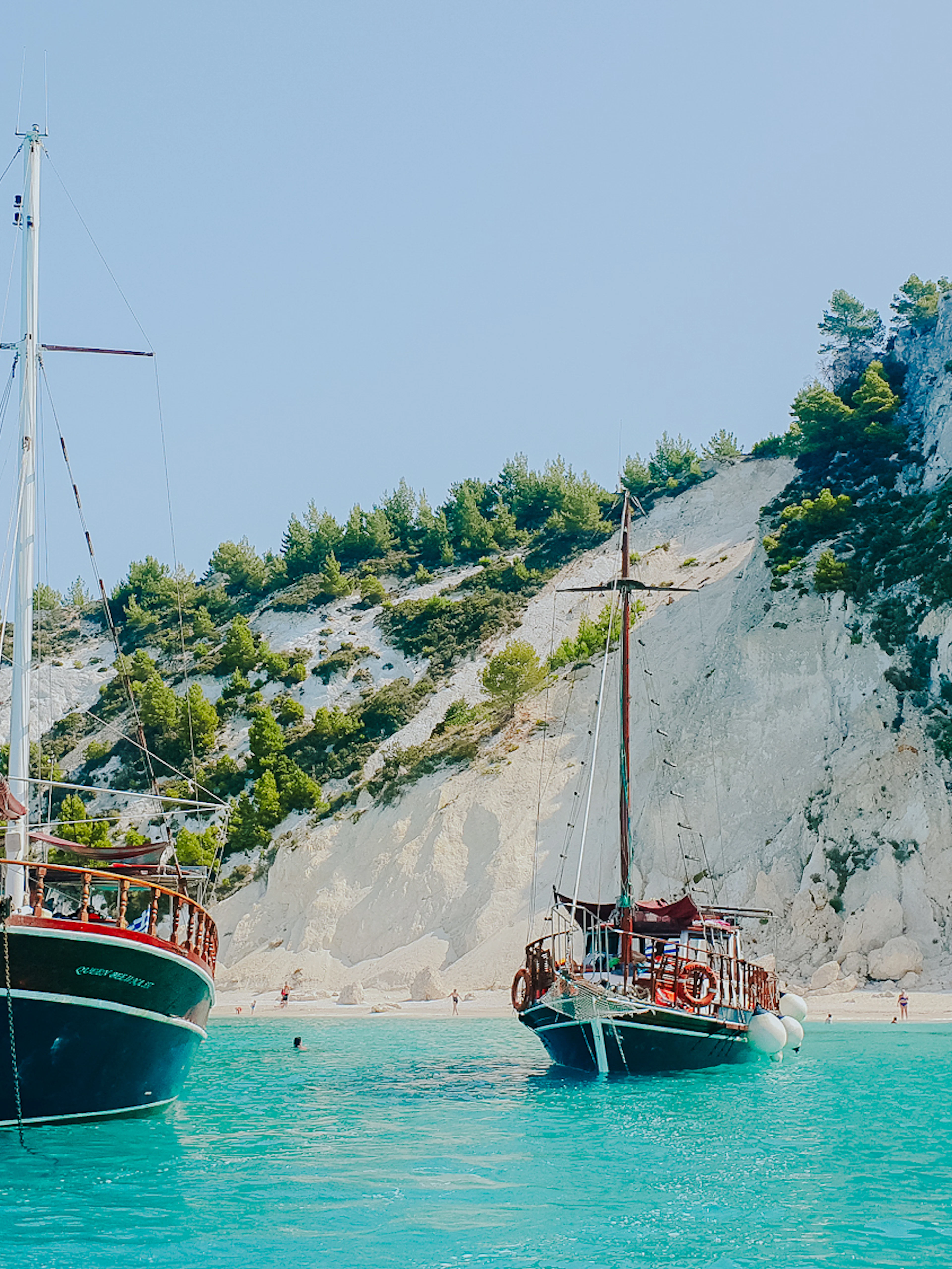 Wooden boats anchored near rocky cliffs and beach in Kefalonia, Greece.