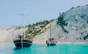 Wooden boats anchored near rocky cliffs and beach in Kefalonia, Greece.