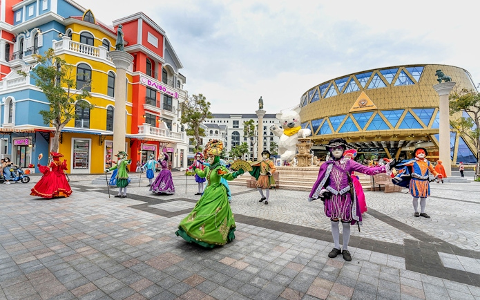 Performers in colorful costumes at VinWonders theme park, Vietnam, near a large bear statue.