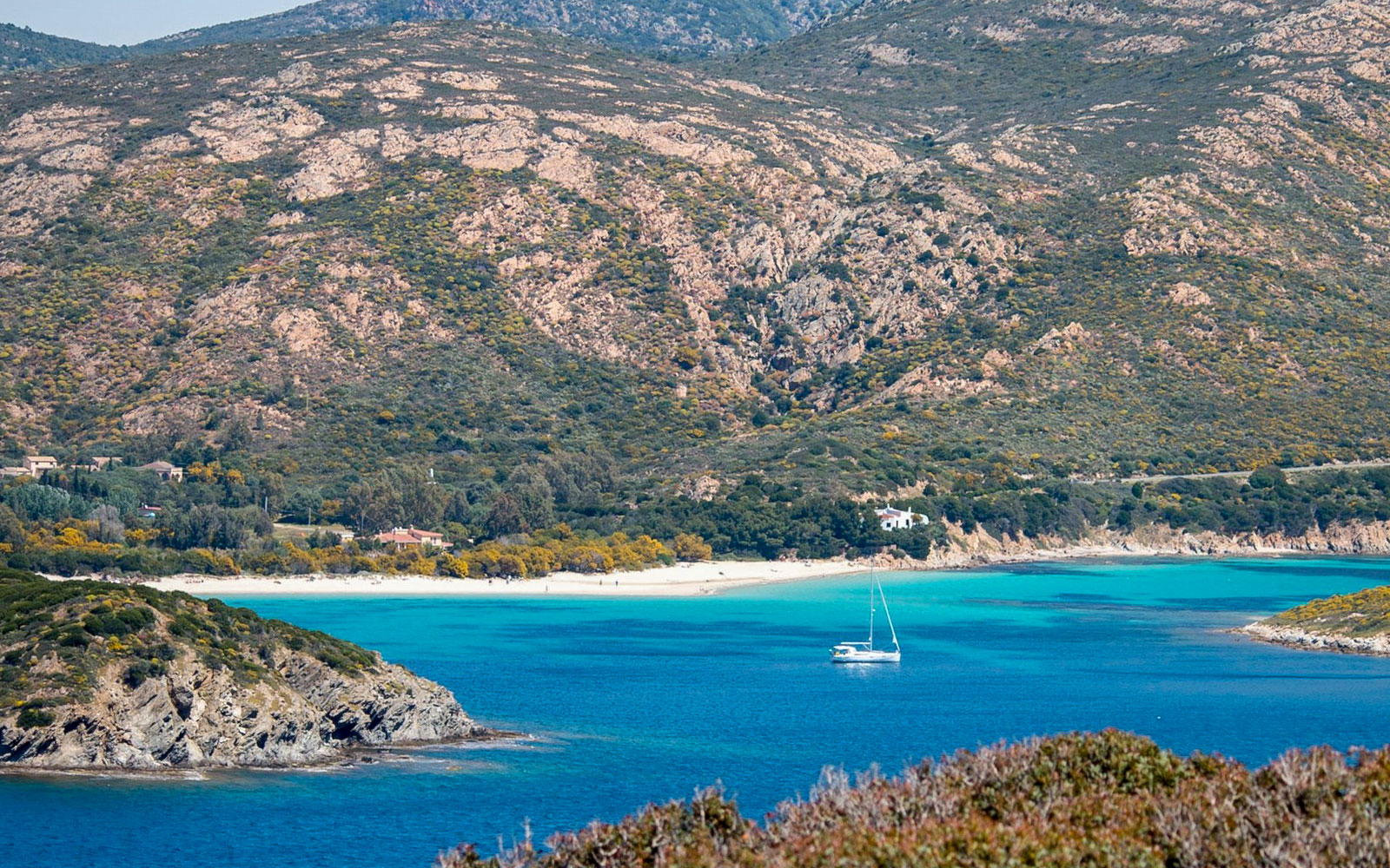 Sailboat on turquoise waters near Chia beach with mountainous backdrop, Cagliari 4x4 tour.