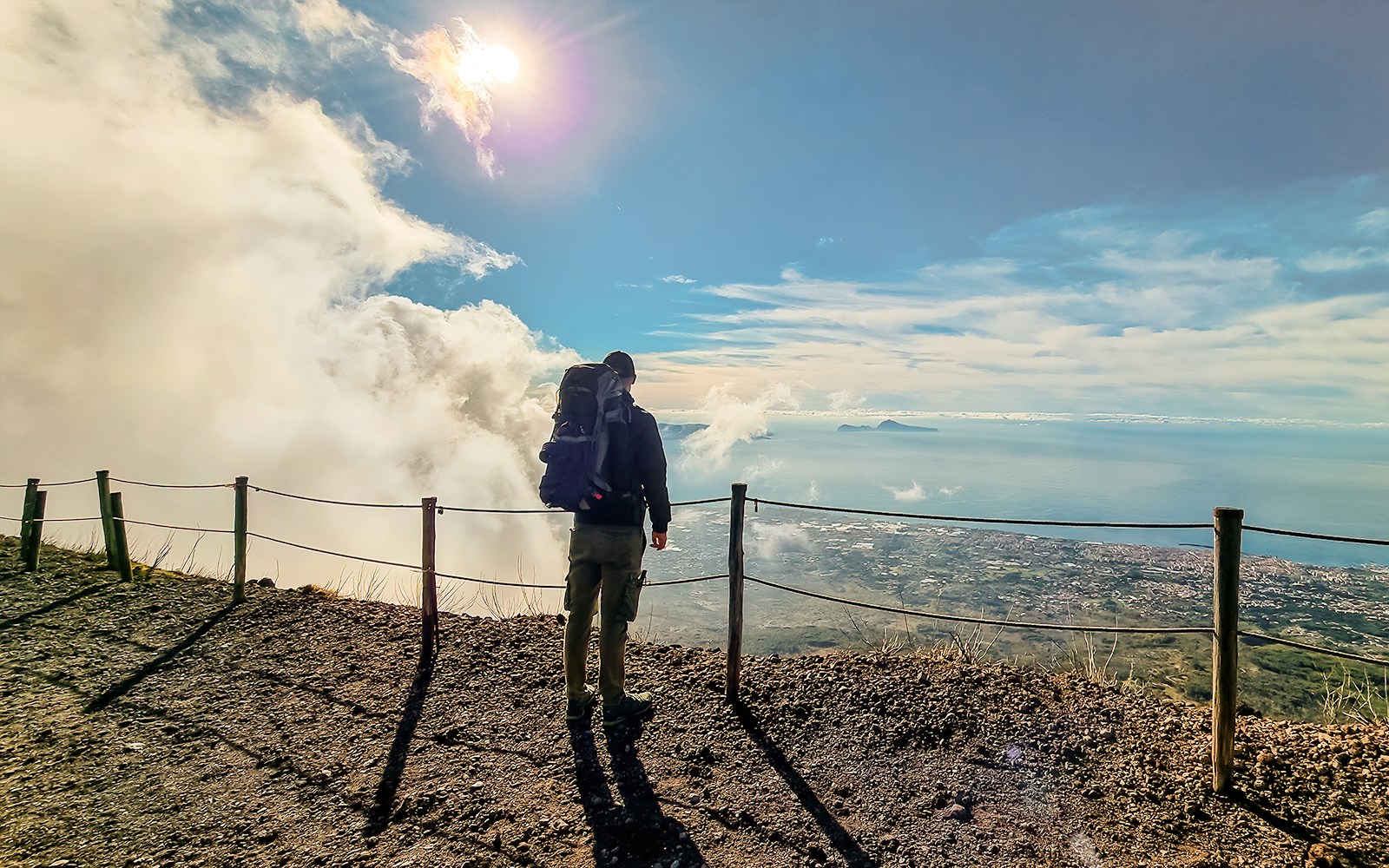 Hiker walking along rocky trail on Mount Vesuvius with view of crater in background, Italy.