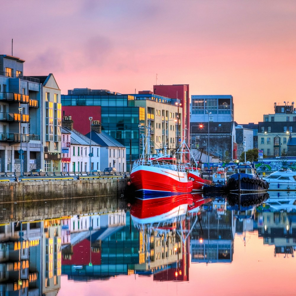 Row of buildings and fishing boats at docks during sunrise in Galway.