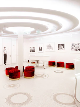 White room with red stools, circular ceiling design, and a white piano at Wintergarten Varieté.