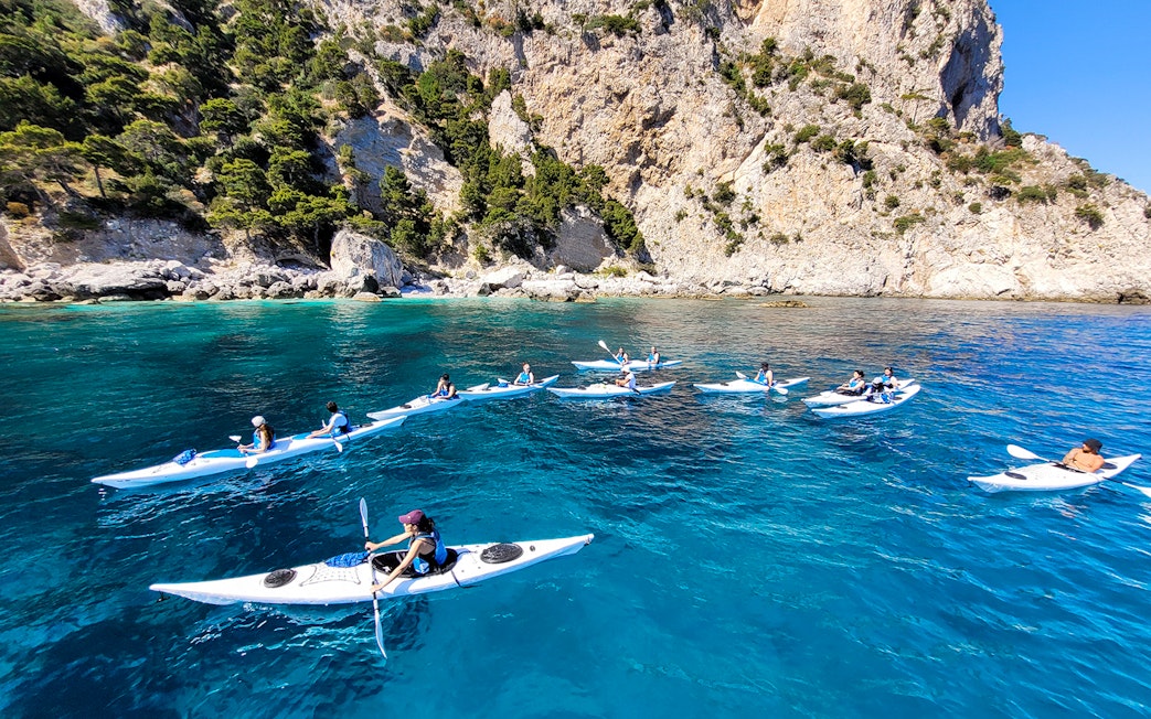 Kayakers exploring Capri's coastline near rocky cliffs and clear blue water.