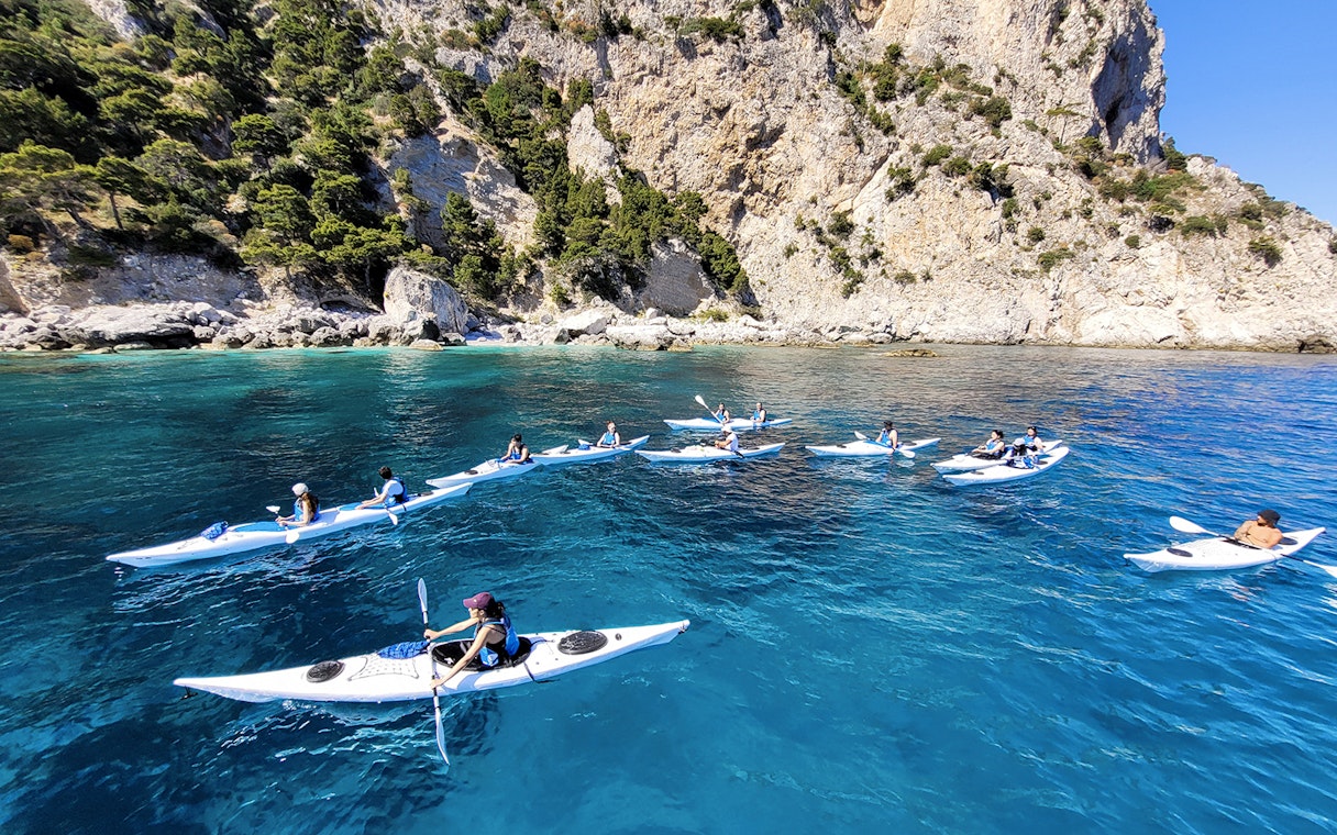 Kayakers exploring Capri's coastline near rocky cliffs and clear blue water.