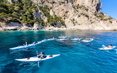 Kayakers exploring Capri's coastline near rocky cliffs and clear blue water.