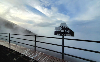Mt. Fuji summit sign at 3,250 meters with misty clouds and wooden pathway.