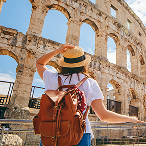 Traveler admiring the Colosseum in Rome, Italy, wearing a backpack and straw hat.