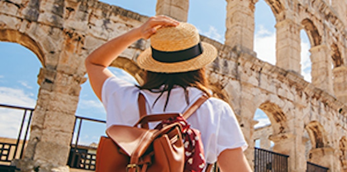 Traveler admiring the Colosseum in Rome, Italy, wearing a backpack and straw hat.