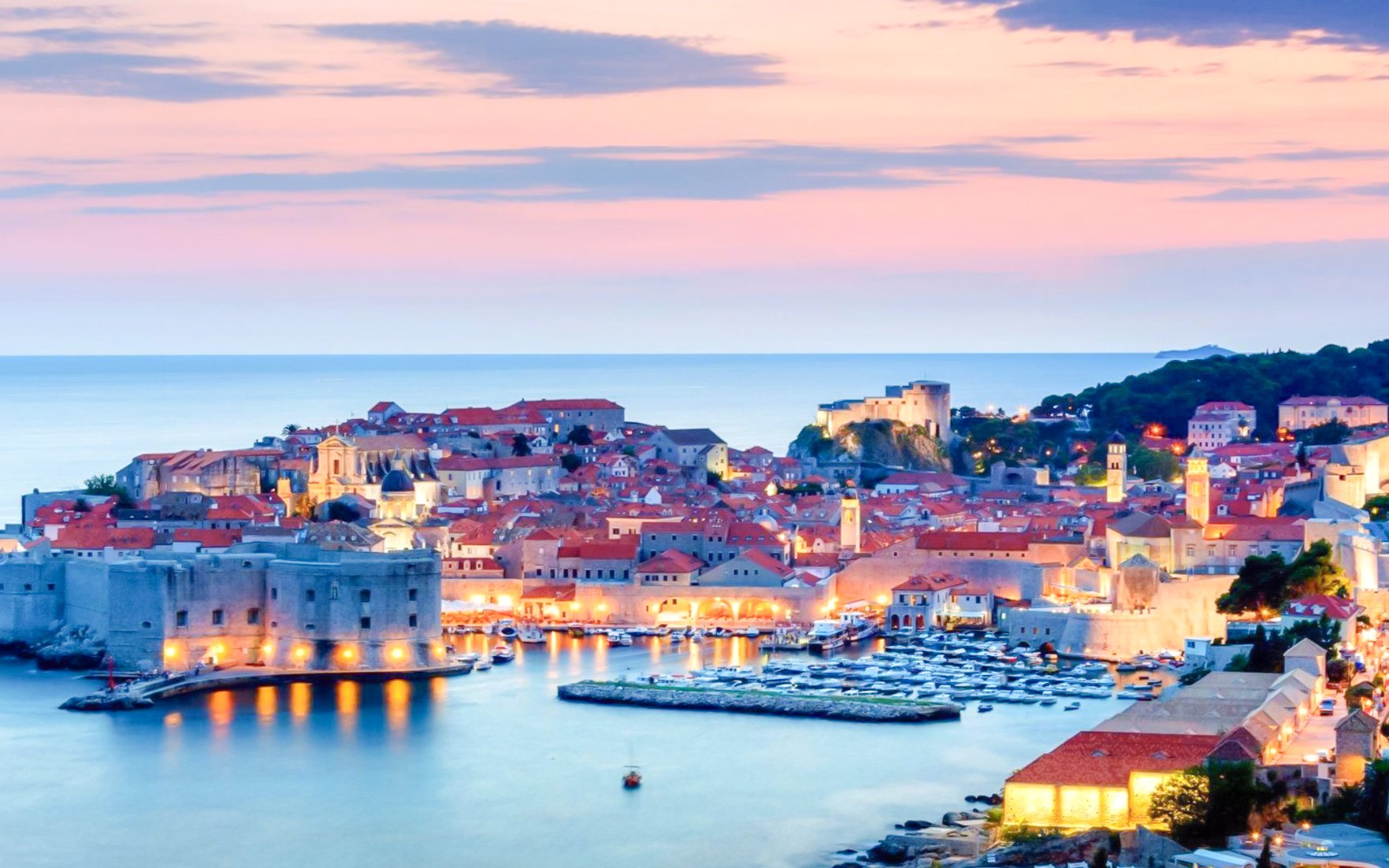 Dubrovnik Old Town at sunset with illuminated city walls and harbor.