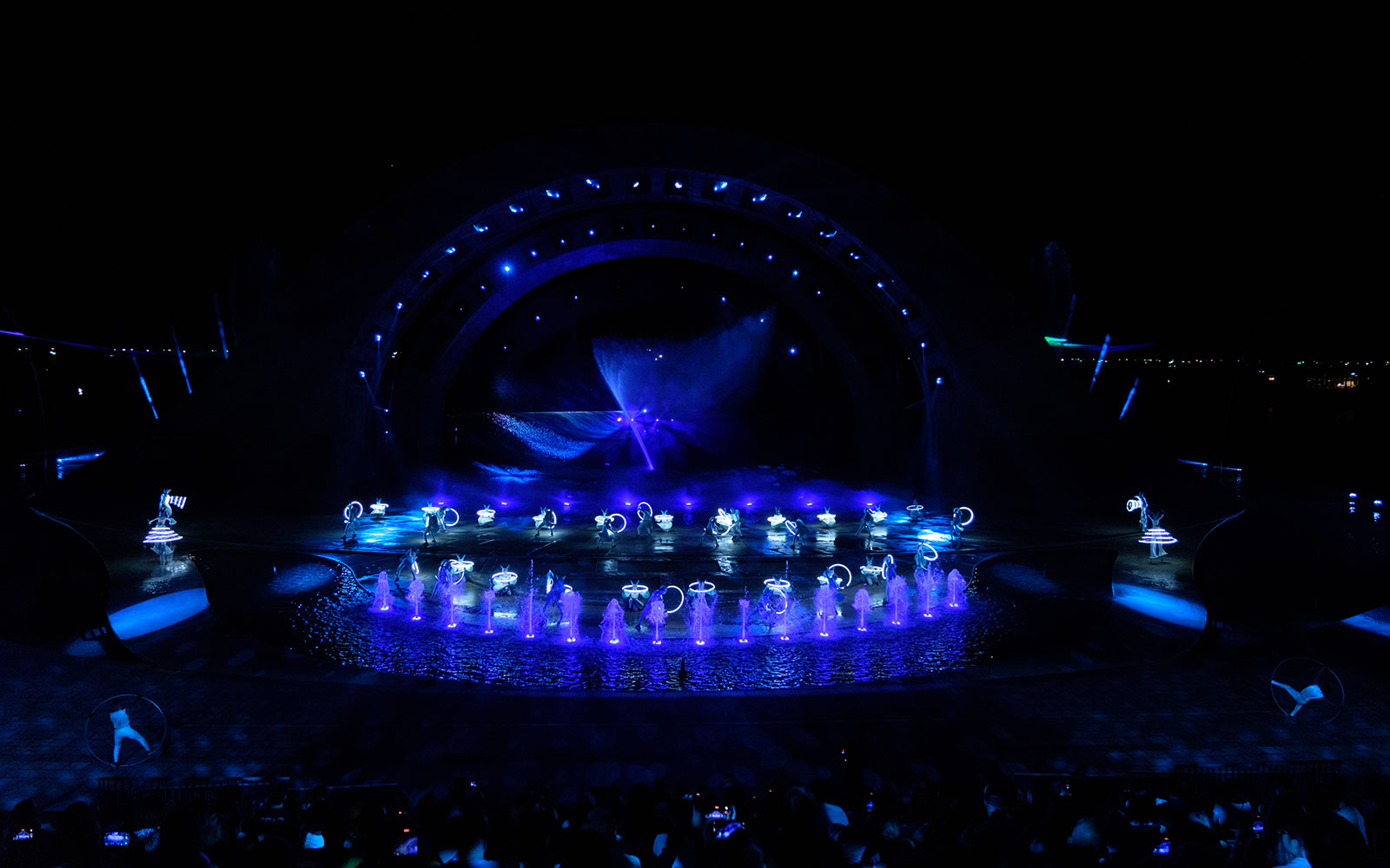 Performers with glowing props in a water-themed stage show, Kiss of the Sea.