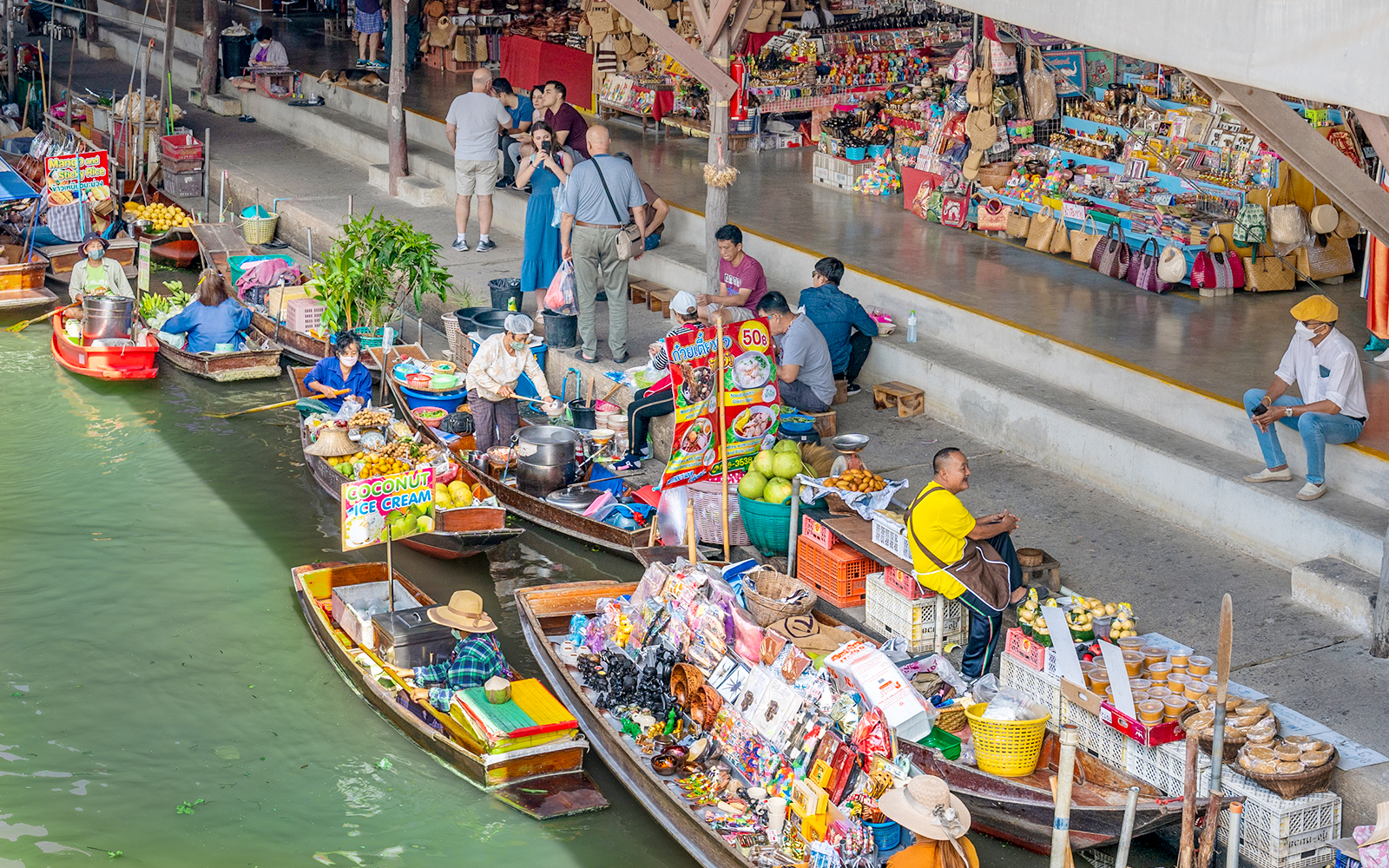 Boats selling goods at Damnoen Saduak Floating Market, Thailand, with vendors and tourists.