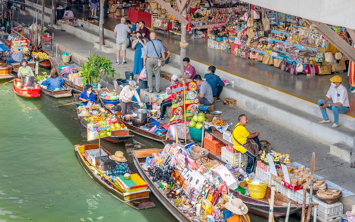 Boats selling goods at Damnoen Saduak Floating Market, Thailand, with vendors and tourists.