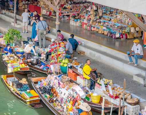 Boats selling goods at Damnoen Saduak Floating Market, Thailand, with vendors and tourists.
