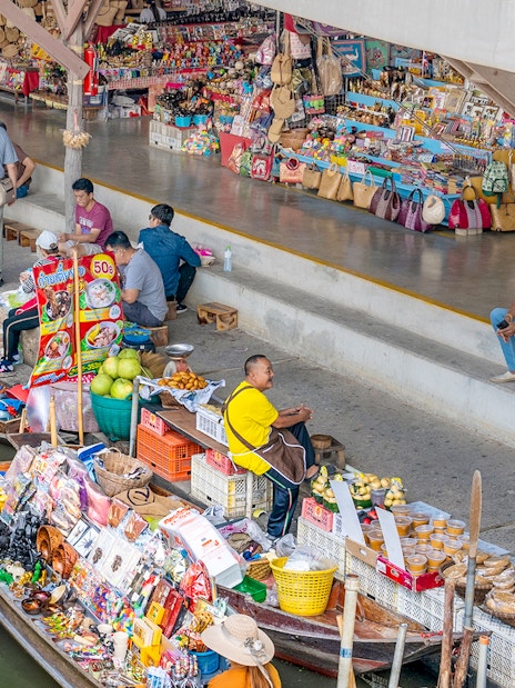 Boats selling goods at Damnoen Saduak Floating Market, Thailand, with vendors and tourists.