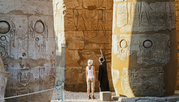 Private guide and tourist explore sandstone columns at Karnak Temple, Luxor, Egypt.