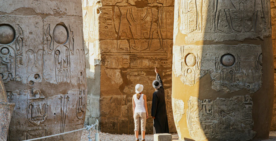 Private guide and tourist explore sandstone columns at Karnak Temple, Luxor, Egypt.