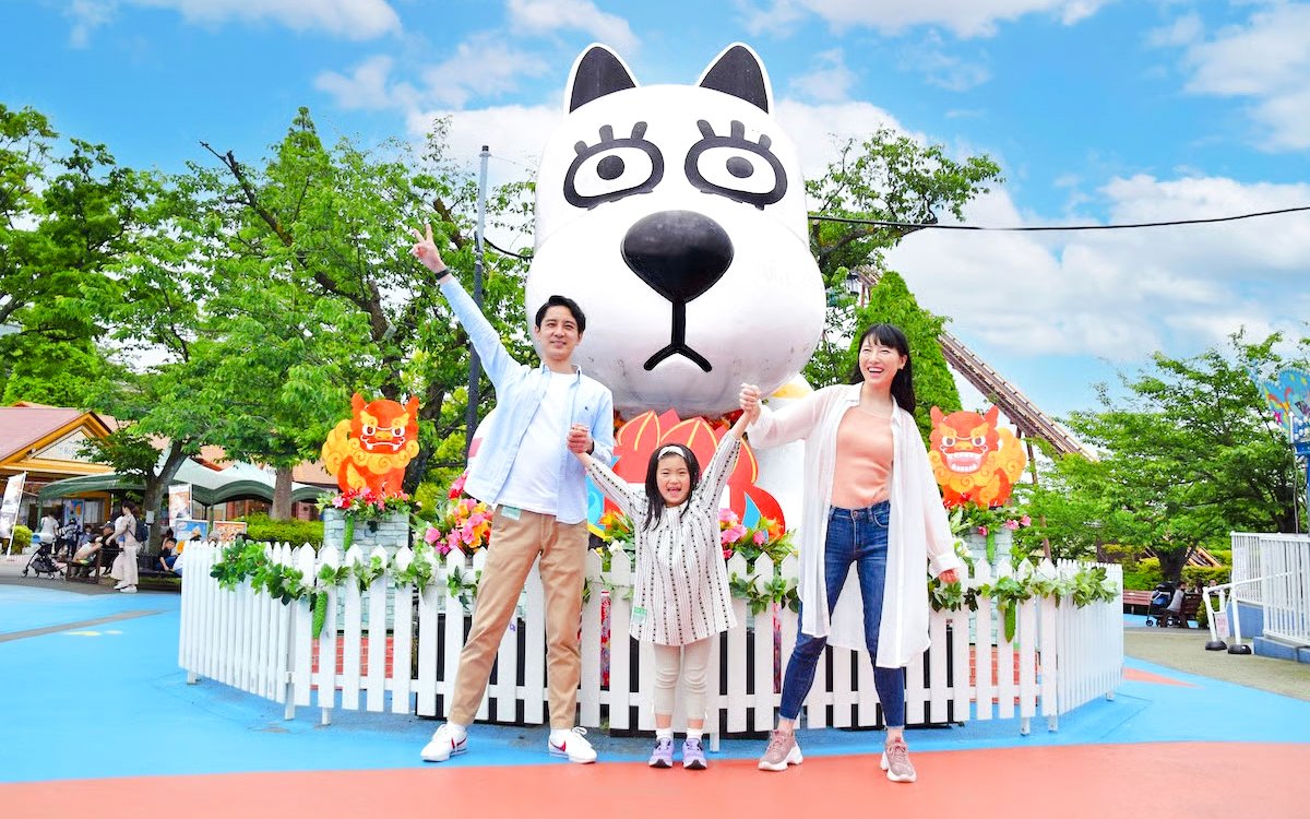 Family enjoying Yomiuriland amusement park in Tokyo with a large cartoon character statue.