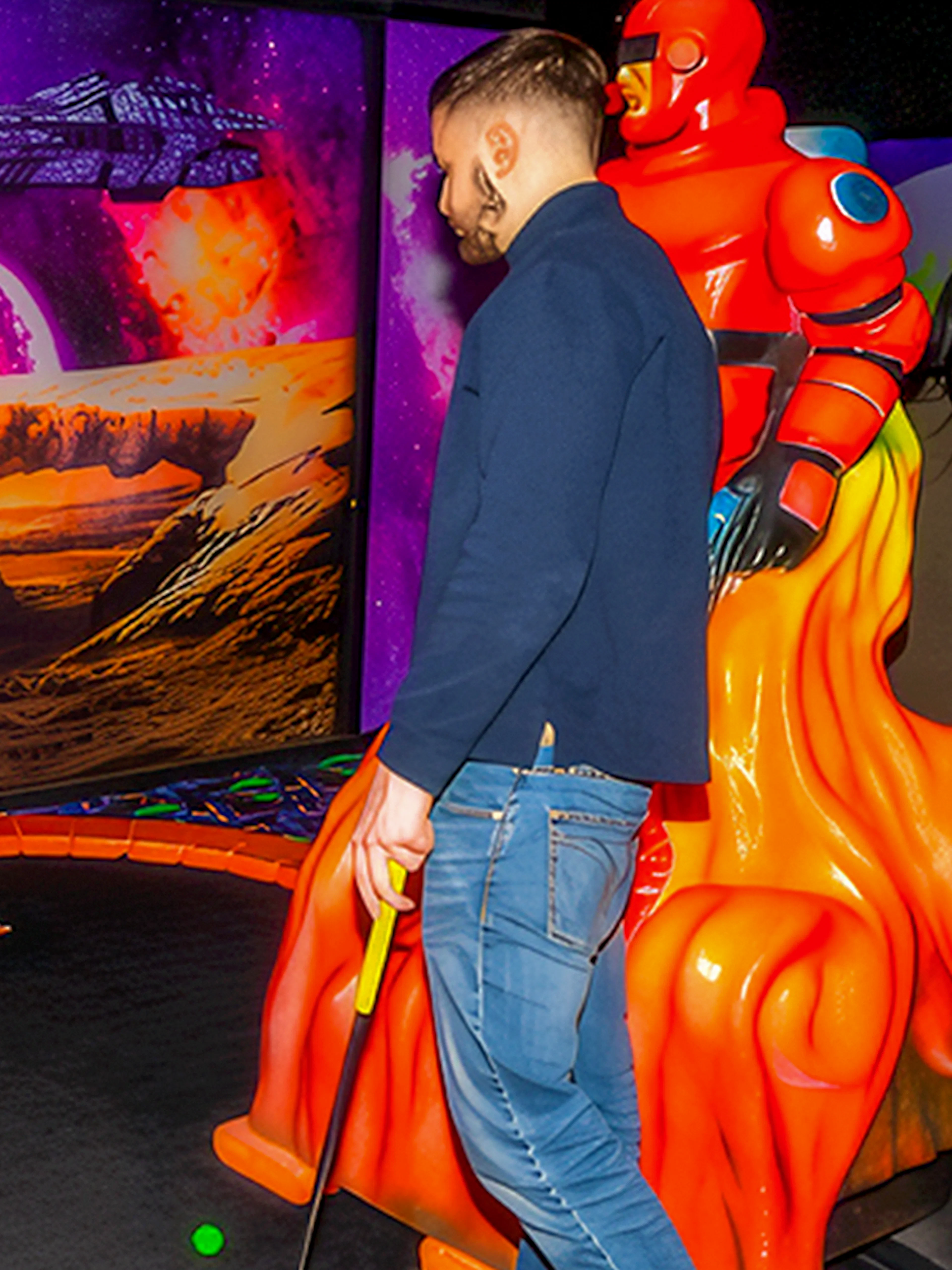 Guests playing mini golf under blacklight with a sci-fi themed backdrop.