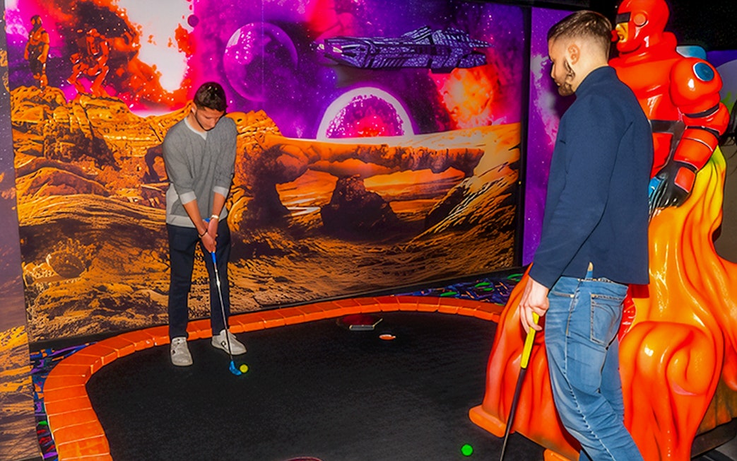 Guests playing mini golf under blacklight with a sci-fi themed backdrop.