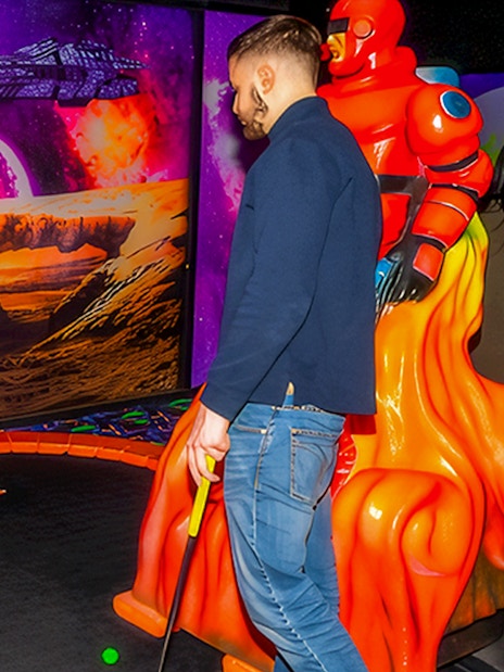 Guests playing mini golf under blacklight with a sci-fi themed backdrop.